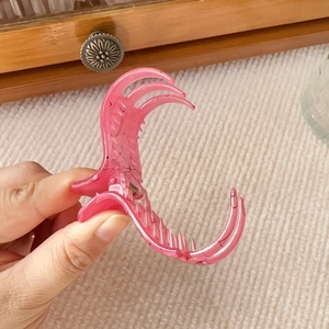 Detail of a pink translucent shark hair claw clip held by hand for a size reference