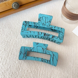 Dettaglio di grandi mollette per capelli azzurre con texture nera su tessuto bianco