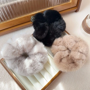 Detailed plush faux mink hair scrunchies in black, grey, and khaki on a wooden tray