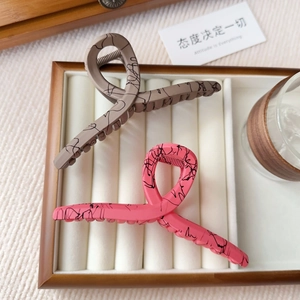 Detail of matte hair claws in pink and grey with black ink texture on a wooden tray