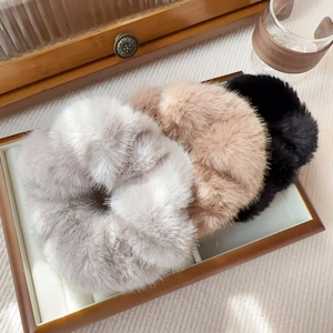 Close-up of soft faux mink fur scrunchies in grey, pink, and black on a wooden tray