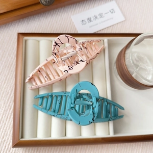Detail of large marble patterned acetate shark hair clips in pink and teal green