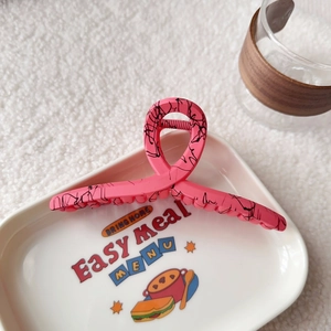 Close-up of pink shark hair claw clip with black marble pattern on white tray