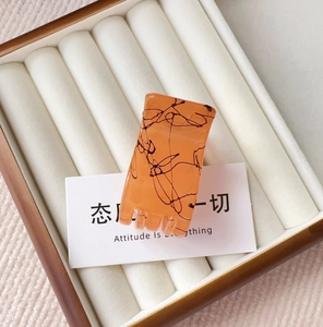 Detail view of amber orange resin hair claw clip with black marble texture in a jewelry box