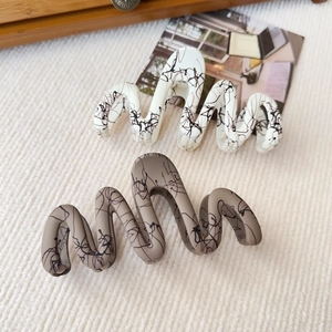 Detail view of large wavy hair claws in cream and taupe with artistic black ink patterns