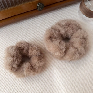 Macro shot of soft faux mink fur scrunchies in khaki on a textured white fabric background