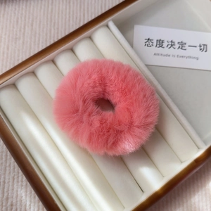 Close-up of a fluffy pink plush scrunchie displayed on a white velvet jewelry box base