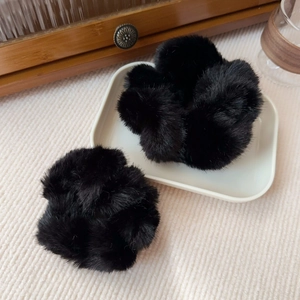 Close-up of two thick black plush faux fur scrunchies on a minimalist white ceramic tray