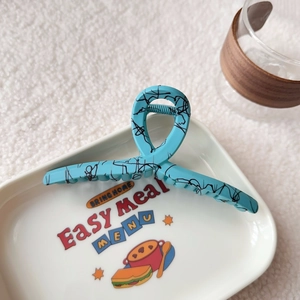 Detail of sky blue matte hair claw clip with black graffiti lines on white decorative tray