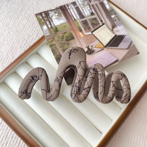 Detail of khaki wavy hair claw clip with black abstract lines on a jewelry box