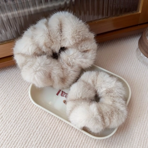 Macro detail of plush beige faux mink fur scrunchies showing soft texture in a tray