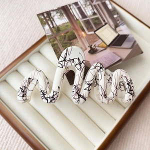 Detail view of wavy cream hair claw clip with black ink patterns in a jewelry box
