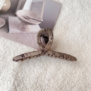 Detailed view of beige shark hair clip with black abstract lines on soft textured fabric