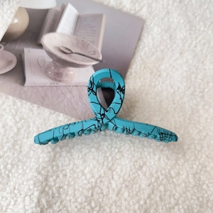 Macro view of a large cyan claw clip with black abstract ink patterns on white wool