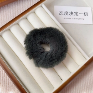 Close-up of a soft grey faux fur hair tie displayed in a white velvet jewelry box