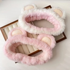 Detailed view of two cute plush coral fleece headbands in pink and white on a wooden tray