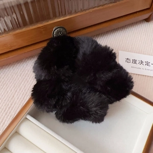 Detail view of a black faux mink fur scrunchie with a vintage metal buckle on white tray