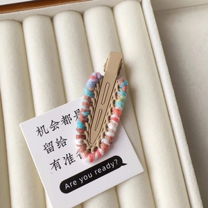 Detail of hand-woven colorful wool yarn on a matte khaki alloy duckbill hair clip