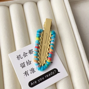 Close-up of a handmade knitted duckbill hair clip with colorful yarn details on beige card