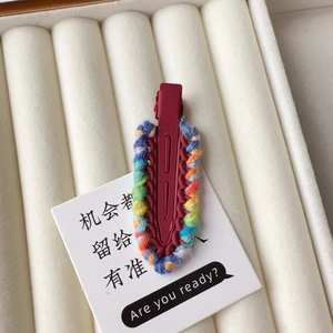 Macro view of a colorful hand-knit wool duckbill hair clip in a white velvet jewelry box
