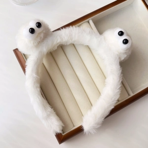 Close-up of white plush monster headband with big round eyes in wooden jewelry box