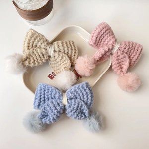 Gros plan de barrettes à nœuds tricotés avec pompons en beige, rose et bleu clair
