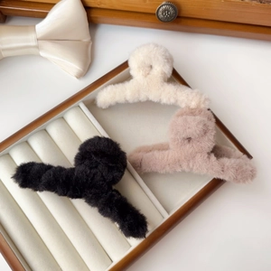 Three plush hair claws in cream, pink, and black colors displayed on a wooden tray