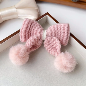 Détail de barrette nœud tricoté rose avec pompons en fourrure sur plateau velours