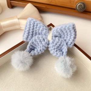 Vue détaillée d'une pince à cheveux avec nœud en tricot bleu et pompons en peluche