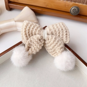 Détail d'une pince à cheveux nœud en tricot crème avec pompons blancs doux pour l'hiver