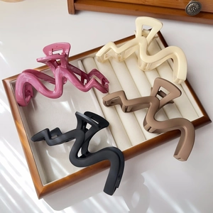 Detail of four matte wavy hair claws in pink, beige, coffee and black on a tray