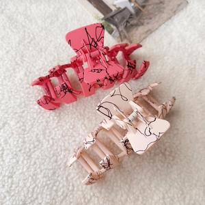 Detail of pink and cream matte hair claws with black graffiti lines on soft plush background