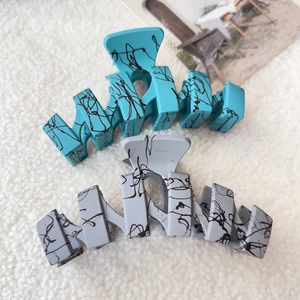 Detail of matte hair clips in blue and grey with artistic black graffiti patterns