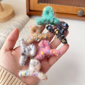 Détail de six mini pinces à cheveux en peluche colorées tenues à la main dans un décor chaleureux