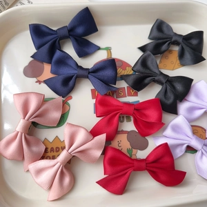 Detail of satin bow hair clips in navy, black, pink, red and purple on a white tray