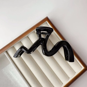 Close-up of black glossy wave hair claw clip on white velvet display tray with wood frame