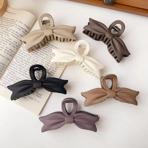 Flat lay of six large matte bow hair clips in neutral earth tones on white background