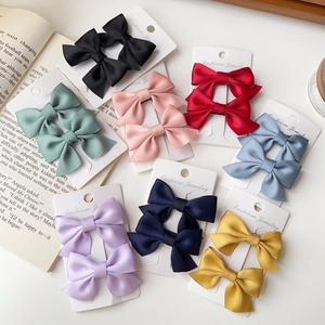 Set of 2 satin bow hair clips in multiple colors on jewelry cards with a book background