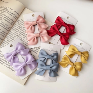 Flat lay of colorful satin bow hair clips in pink, red, and blue on white cardboards