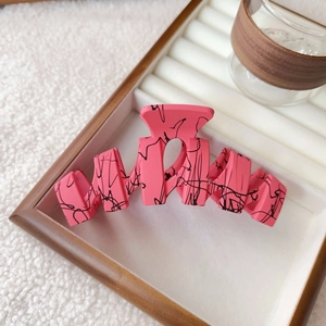 Detail view of large matte pink hair claw with black ink marble texture and wavy design