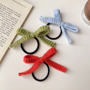 Nahaufnahme von drei gestrickten Schleifen-Haargummis in Blau, Grün und Korallenrot