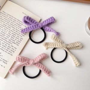 Detailansicht von lila rosa und cremefarbenen gestrickten Schleifen-Haargummis auf Buch.