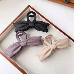 Detail view of three matte bow hair claws in black, mauve, and beige on a velvet tray