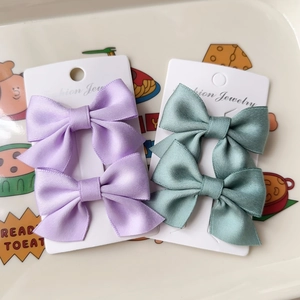 Set of two pairs of satin bow hair clips in lavender and sage green colors on a card