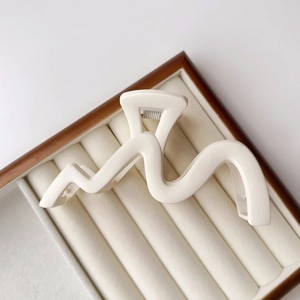 Detail of a matte cream-colored wavy hair claw clip resting on a velvet jewelry box