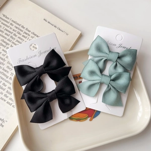 Detail of satin bow hair clips in black and sage green on a cream-colored tray