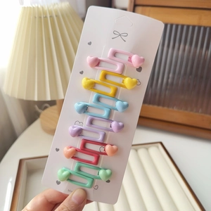 Détail de six barrettes colorées pour enfants avec décorations de cœur sur carte