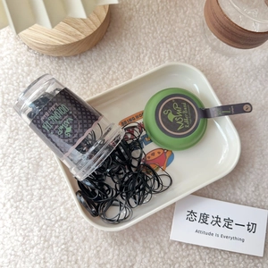 Detail of black rubber hair bands in a transparent jar on a white ceramic tray