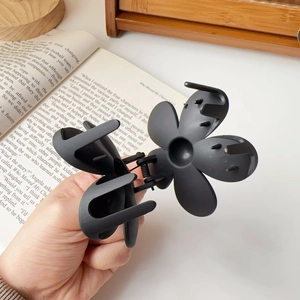 Detail of a matte black flower-shaped hair claw clip with multi-tooth grip and metal spring