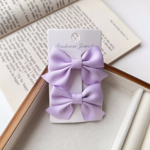 Close-up of purple satin bow hair clips on a jewelry display card with a book background